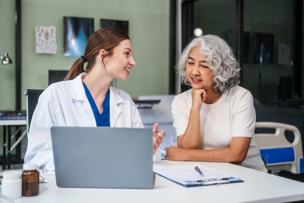 Monthly health check-ups and counseling sessions are provided to an elderly Asian woman by a Caucasian female caregiver, offering support, advice, and motivation.