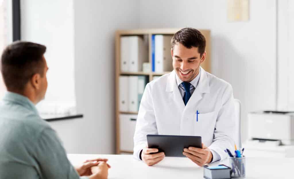 medicine, healthcare and technology concept - doctor with tablet pc computer and male patient talking at medical office in hospital