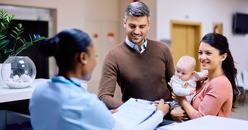 Couple and baby checking in with doctor ay front desk for an appointment.
